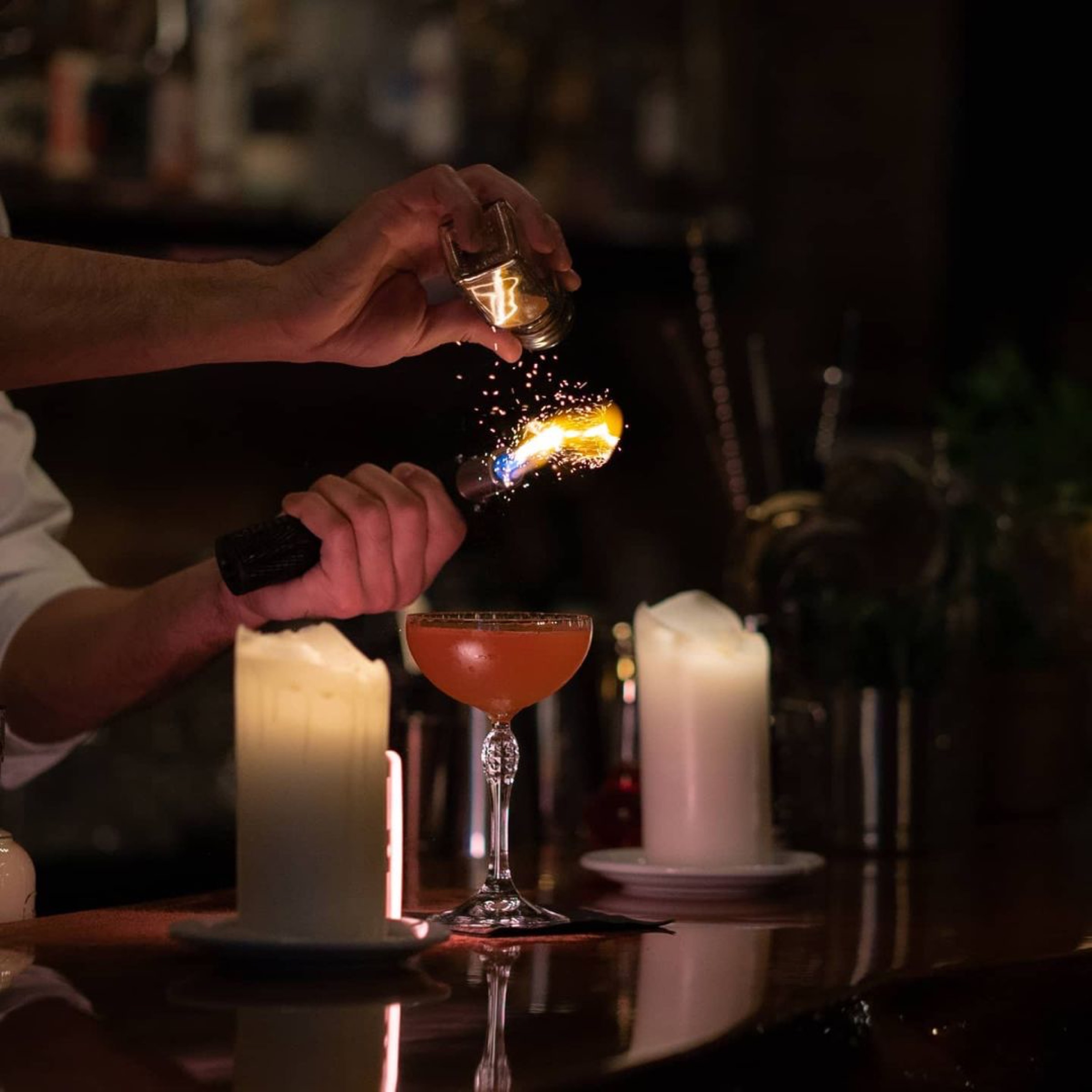 A bartender finishing a cocktail with a flame at Aura
